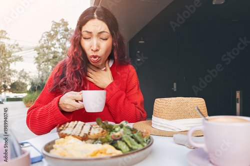 Foto Young woman experiencing pain and choking while drinking hot coffee at an outdoo
