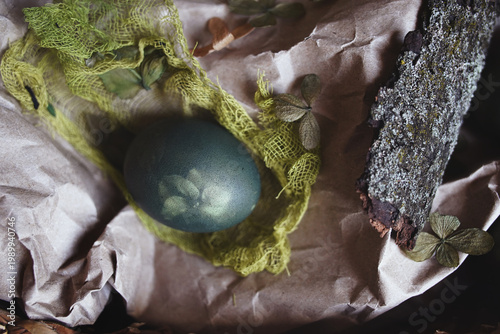 Natural Easter decoration with dried petals, colored egg, craft paper, and tree bark 