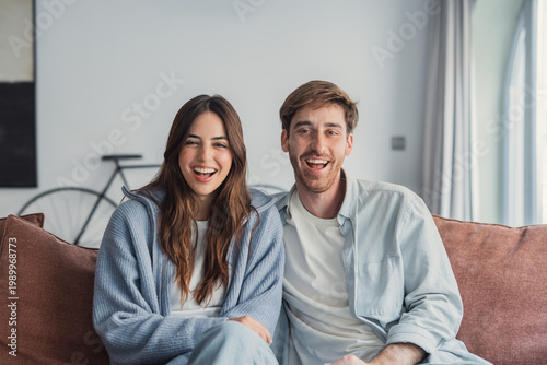 Bild auf Leinwand Young smiling couple relaxing together on a cozy living room couch at home