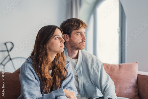 Foto A young couple sits close on a sofa, gazing thoughtfully out a sunlit window