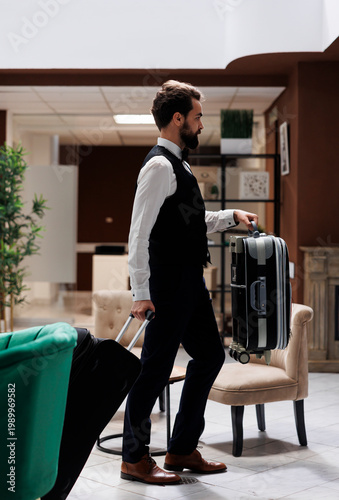 Photography Male hotel concierge carrying bags to help guests in reception area, moving suitcases and tolleys for tourists checking in at luxury resort