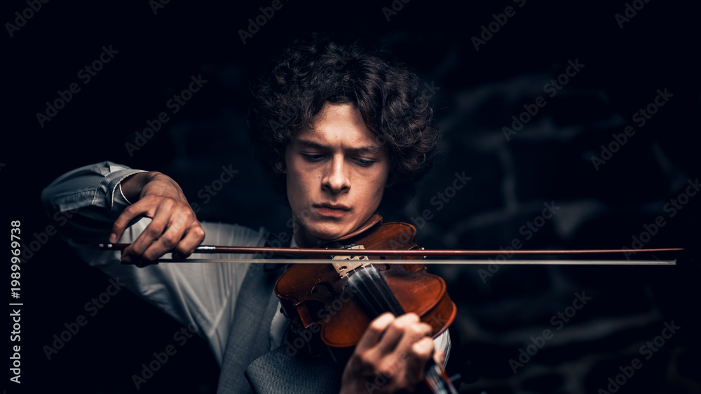 Fototapeta premium Young male violinist playing violin in elegant attire