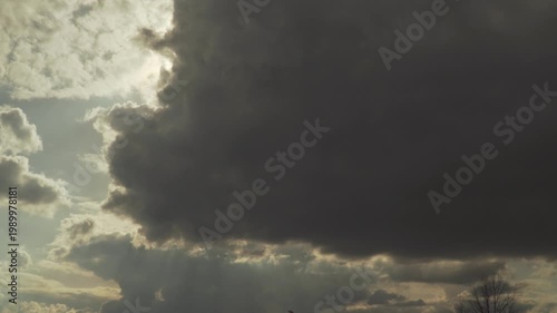 Heavy dark storm clouds dominate the sky as bright sunlight breaks through the edges. Dramatic light rays pierce the atmosphere, creating a powerful and moody celestial display of nature. 