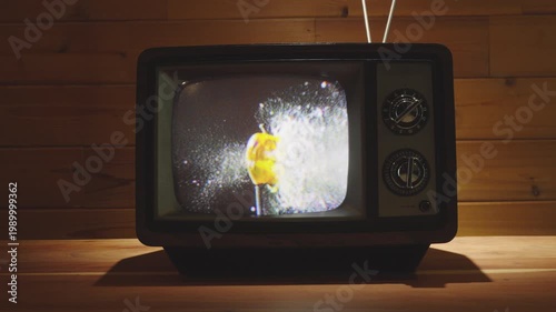 Bullet going through apple appearing on a vintage television in living room with wooden background. 