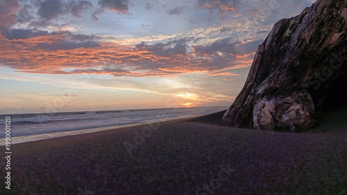 Dramatic sunset over a sandy beach with a large driftwood log and colorful clouds, perfect for travel promotions, coastal landscapes, and nature backgrounds.