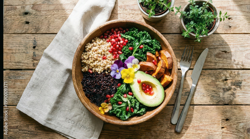 Healthy food bowl with quinoa, black rice, kale, avocado, sweet potato, pomegranate seeds, and edible flowers on rustic wooden table with cutlery and potted plants