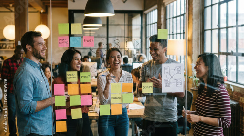 Startup team brainstorming with colorful sticky notes on glass wall, diverse young professionals laughing and collaborating in modern office space filled with natural light and industrial decor