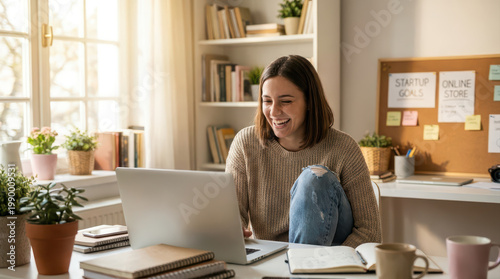 Young woman working on laptop at home office, smiling and enjoying remote work with cozy interior and natural light, surrounded by plants and books
