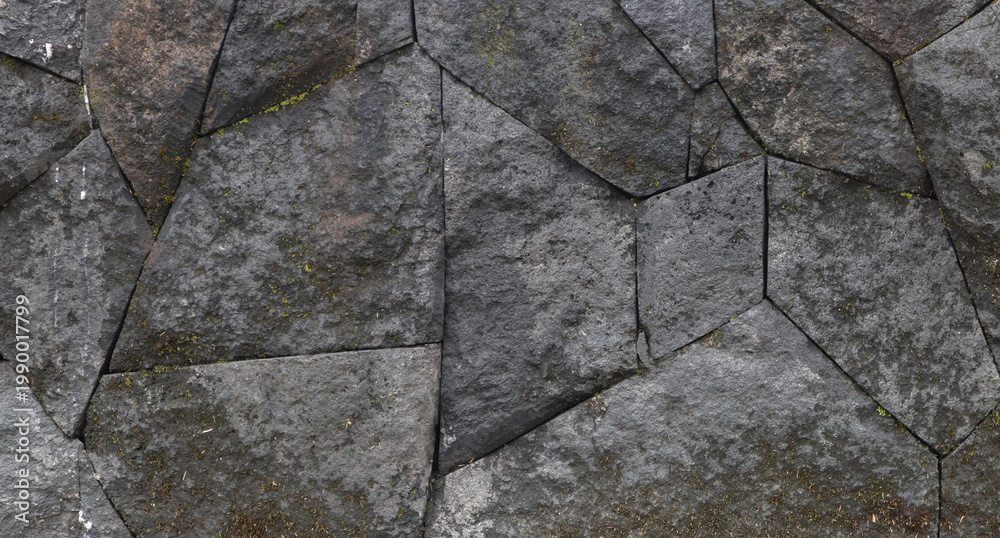 Obraz premium Weathered dark gray stone wall with intricate polygonal masonry pattern; ancient outdoor surface texture background