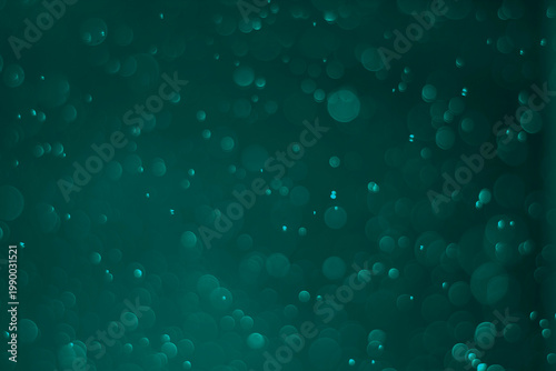 Blurred abstract background with sparkling Teal bokeh on a dark background.