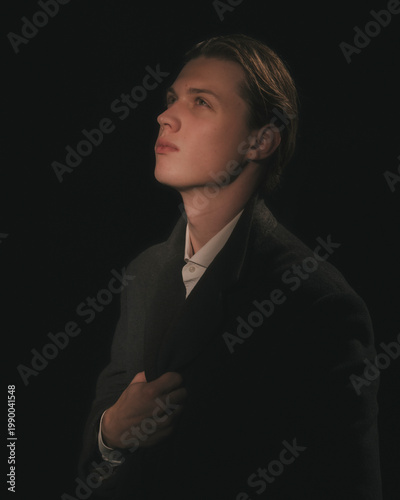 Blonde man in white shirt and charcoal blazer lifts gaze upward in sublime yearning three quarter profile moody poetic editorial studio menswear portrait