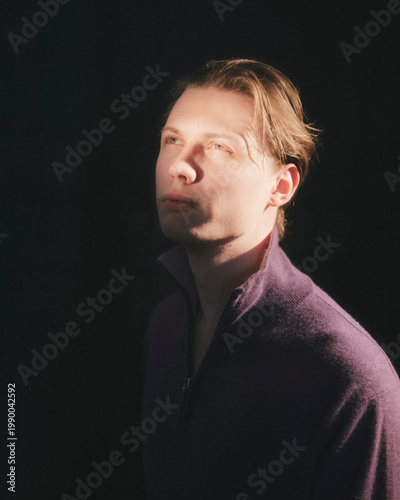 Blonde man in plum purple zip neck sweater looks upward in three quarter profile with yearning aspirational gaze moody poetic cinematic studio editorial portrait
