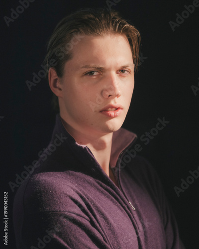 Blonde man in plum purple zip neck sweater faces camera with soft lips and composed direct gaze moody refined sensitive cinematic studio portrait
