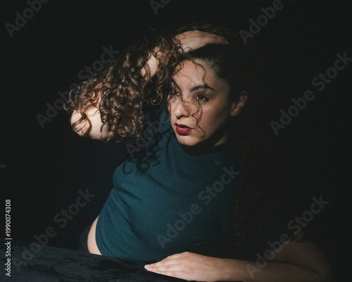This dramatic portrait features a woman with curly hair posing dramatically, evoking emotions of thoughtfulness and allure against a dark background.