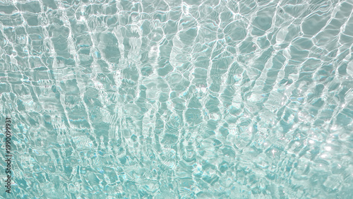 Sunlight reflecting through clear swimming pool water creating abstract caustic patterns on the blue floor. Abstract wallpaper, backdrop, background.
