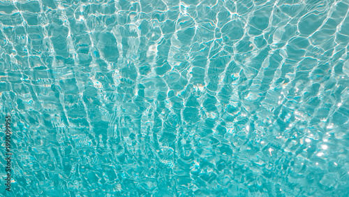 Sunlight reflecting through clear swimming pool water creating abstract caustic patterns on the blue floor. Abstract wallpaper, backdrop, background.