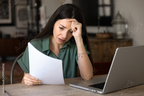 Obraz na plátne Worried woman sitting at table at home holds documents, reading notification from bank, experiencing stress and concerns about huge bills to pay or unpaid taxes