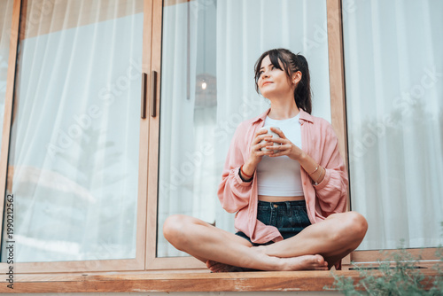 Young woman relaxing on a terrace at home, holding a cup and enjoying a calm moment. Concept of wellness, good health, wellbeing, and balanced lifestyle in a peaceful environment Free Download Young woman relaxing on a terrace at home, holding a cup and enjoying a calm moment. Concept of wellness, good health, wellbeing, and balanced lifestyle in a peaceful environment - GFXLoad