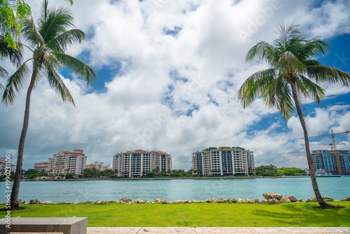 Residential buildings on Fisher Island viewed from Miami beach. Luxury apartment complexes on Fisher Island across the ocean channel with palm trees in the foreground.