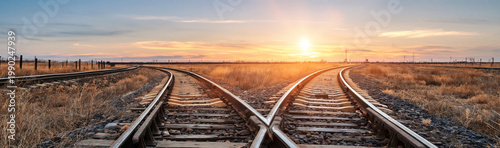 Two railway tracks diverge in a wide open field at sunset with a bright sunflare