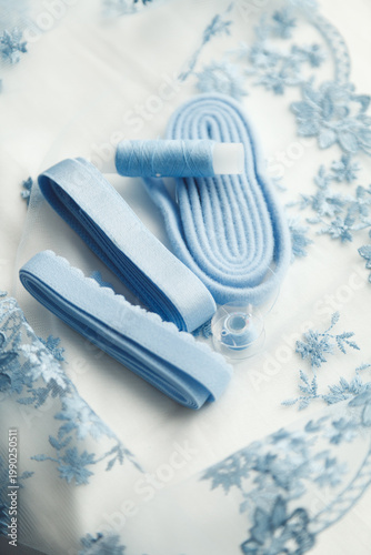 A close-up photo of tailor's tools: blue lace, elastic, spool. Photo grain added.