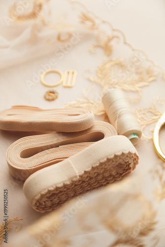 A close-up photo of tailor's tools: beige lace, elastic, spool, accessories for straps, decorations. Photo grain added.