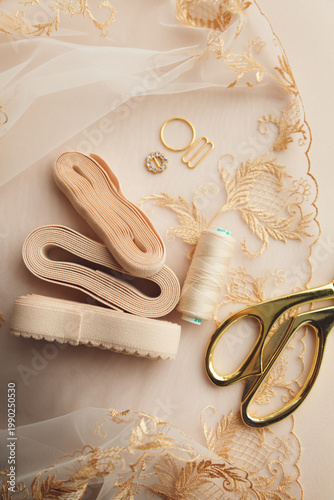 A close-up photo of tailor's tools: beige lace, elastic, spool, accessories for straps, decorations, scissors. Photo grain added.