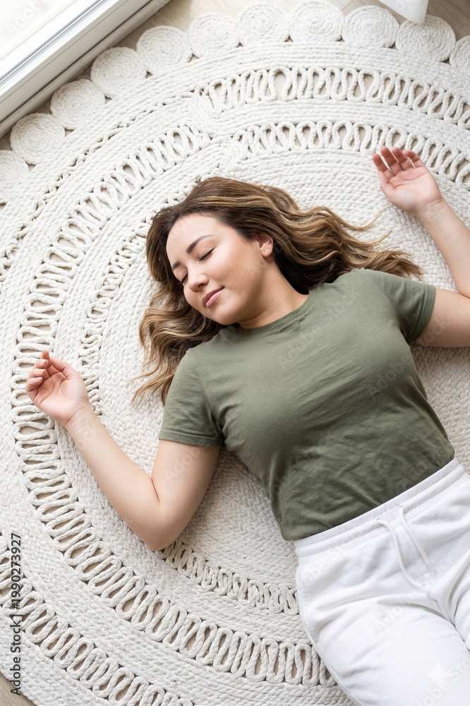 Fototapeta premium Young woman lying on yoga mat with eyes closed and arms open, top view relaxation concept