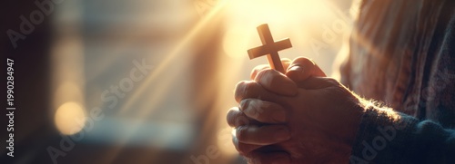 Man holding a wooden cross with clasped hands in sunlight  