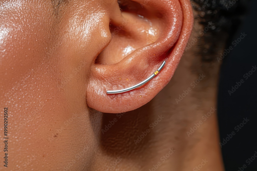 Fototapeta premium Close-up of a person's ear featuring a minimalist silver ear cuff with small orange accents.