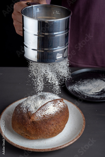 Flour being sifted over rustic bread loaf, artisan baking process