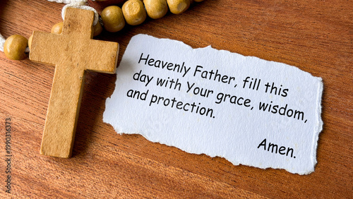 Prayer to heavenly Father text on white prayer note beside wooden cross.