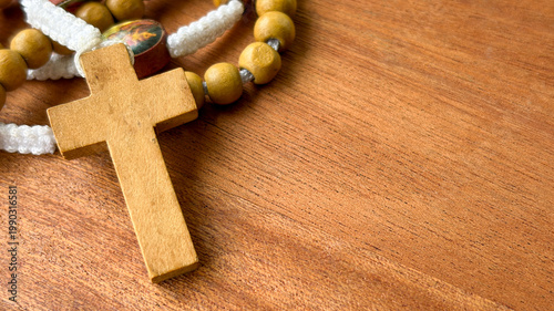 Close view of a wooden cross beside rosary beads on wood symbolizing prayer spirituality and quiet reflection.