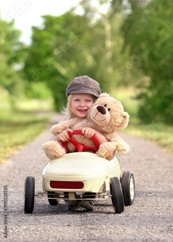 cute girl with her teddy is riding a pedal car