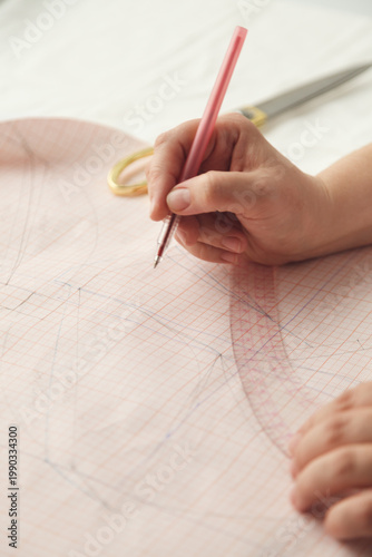 A seamstress draws a pattern using a template. Photo grain added.