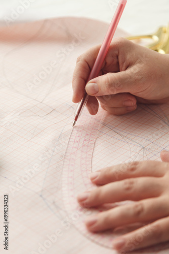 A seamstress draws a pattern using a template. Photo grain added.