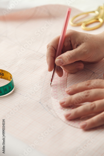 A seamstress draws a pattern using a template. Photo grain added.