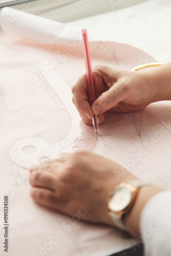 A seamstress draws a pattern using a template. Photo grain added.