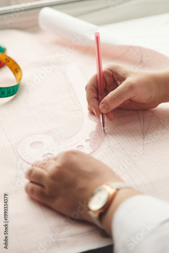 A seamstress draws a pattern using a template. Photo grain added.