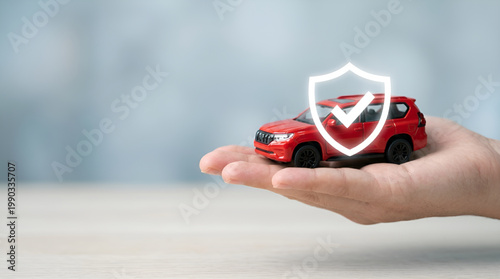 "Hand holding small red toy car with white shield icon for insurance and protection concept. Comprehensive car insurance policy and financial safety for vehicle owners. 
