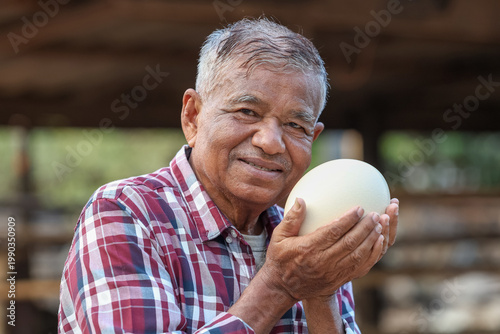 Elderly farmer proudly displays a significant ostrich egg symbolizing sustainable agriculture and the bounty of nature.