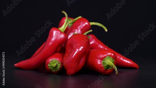 Close-up footage of red capia peppers with green stems on black background.