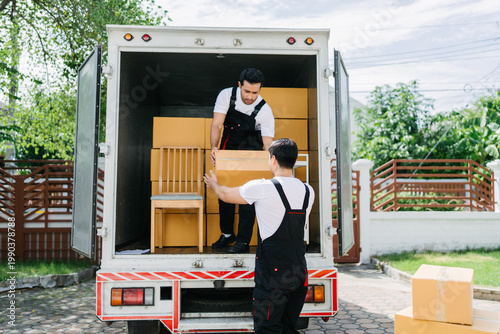 Two male movers unloading cardboard boxes and furniture from a truck in a residential driveway. Professional moving service for home relocation and delivery. Efficient logistics for new home setup