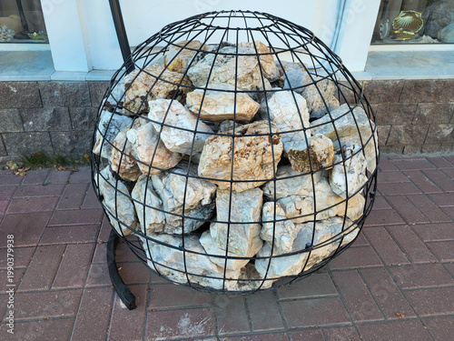 On a city street, there is a round gabion ball filled with colorful stones