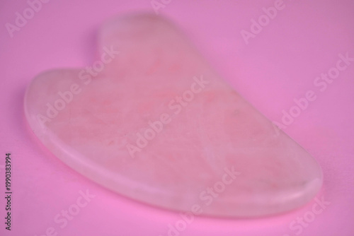 Gouache scraper for facial massage made of rose quartz on a pink background. Close-up.
