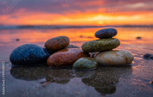 Wet smooth sea pebbles on a sandy beach at sunset with vibrant orange reflections in the water