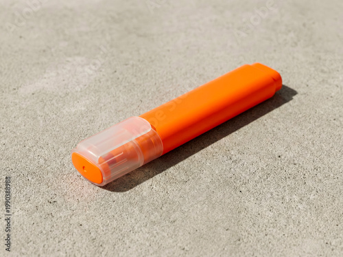 Bright orange permanent marker with a transparent cap lying on a textured concrete surface