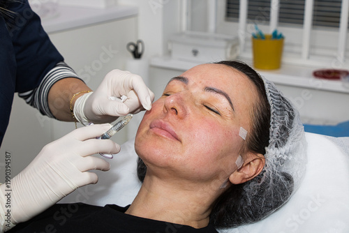 A cosmetologist performs lip augmentation injections on a middle-aged woman.
