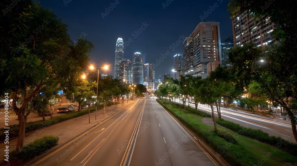 Fototapeta premium A long exposure view of a tree lined urban boulevard passing by modern high rise structures at night