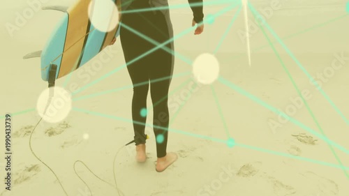 Surfer walking on wet sand, heading to waves, holding board with ankle leash, bokeh lines moving